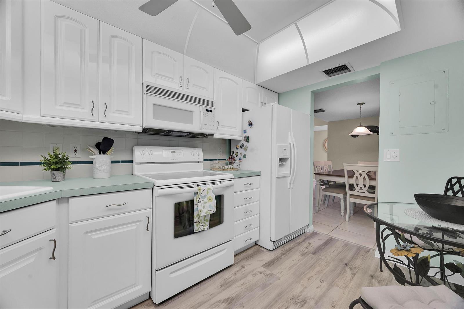 A white kitchen features light green countertops, white appliances, and wood-look flooring — 3492 NE Causeway Boulevard # 103, Jensen Beach FL 34957, JENSEN BEACH, FL