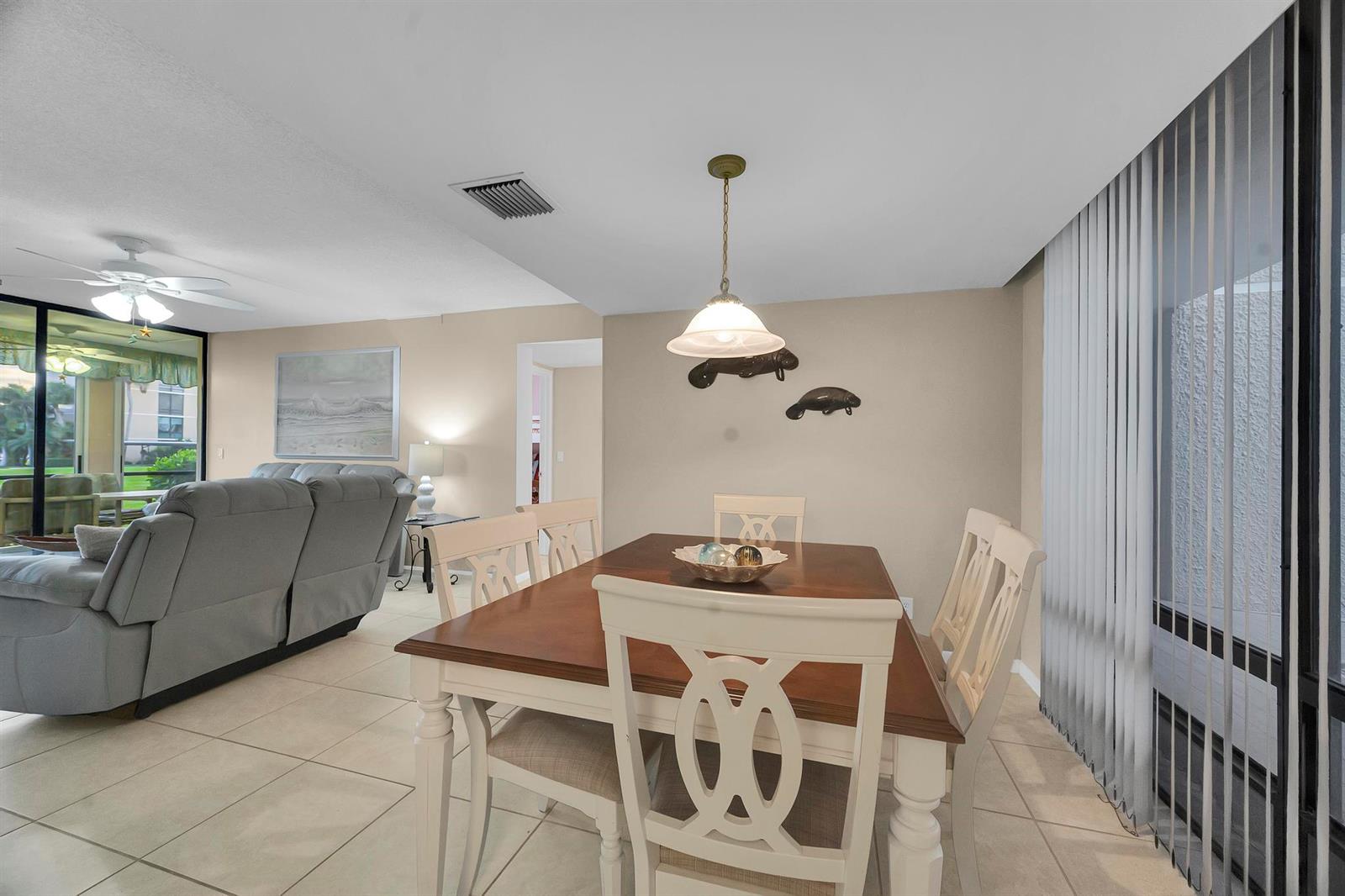 A dining area with a wooden table and chairs sits adjacent to a living room — 3492 NE Causeway Boulevard # 103, Jensen Beach FL 34957, JENSEN BEACH, FL