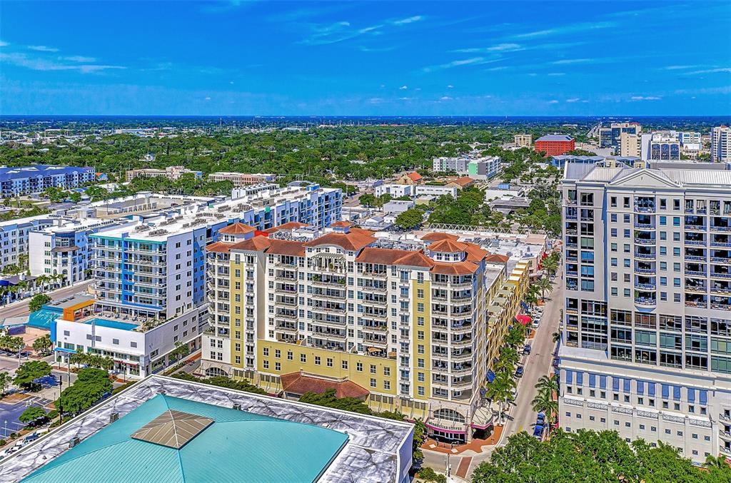 An aerial view shows a multi-story apartment complex with a tan facade and red roof — 100 CENTRAL AVENUE UNIT H716, SARASOTA, FL