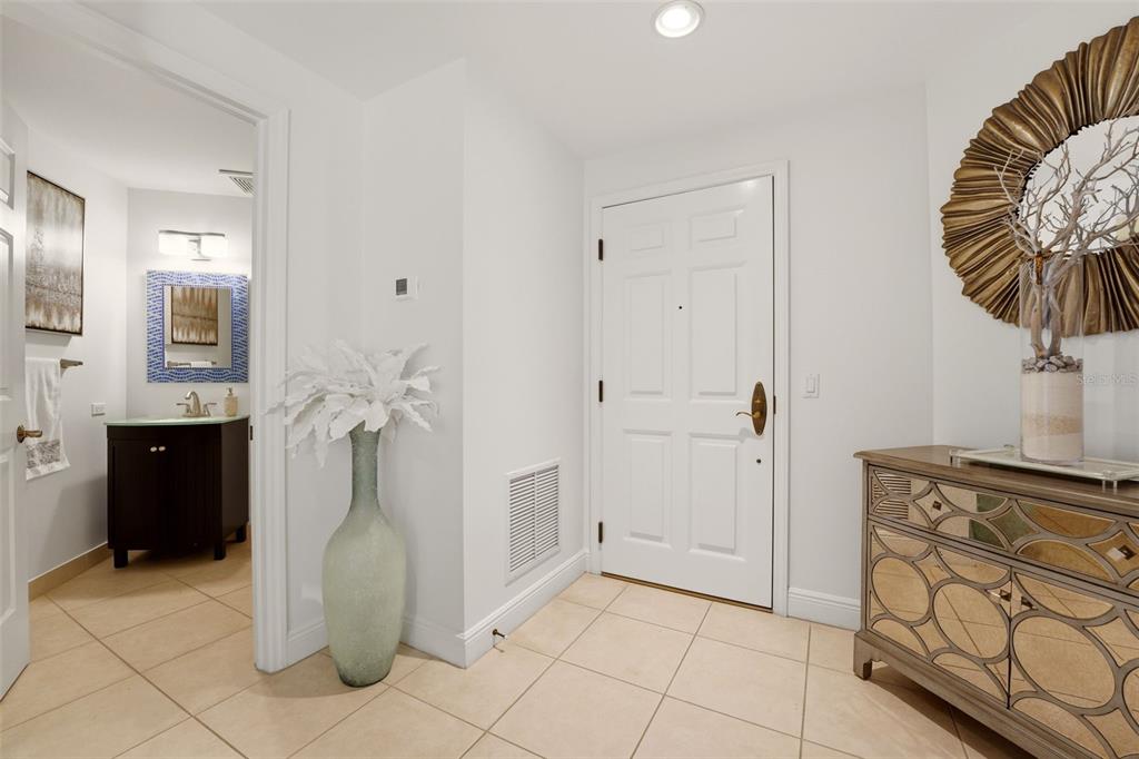 An entryway features a white door, tiled floor, a mirrored chest, and an adjacent bathroom — 100 CENTRAL AVENUE UNIT H716, SARASOTA, FL