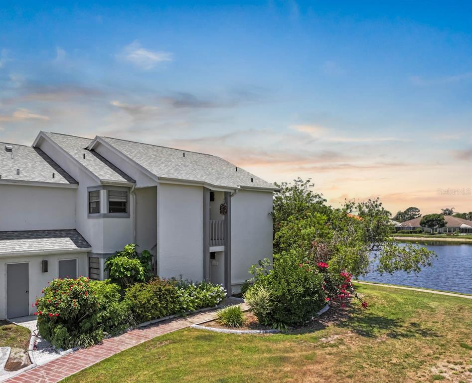 A two-story residential building with a brick walkway and a lake in the background — 609 LIVELY DRIVE UNIT B, SUN CITY CENTER, FL