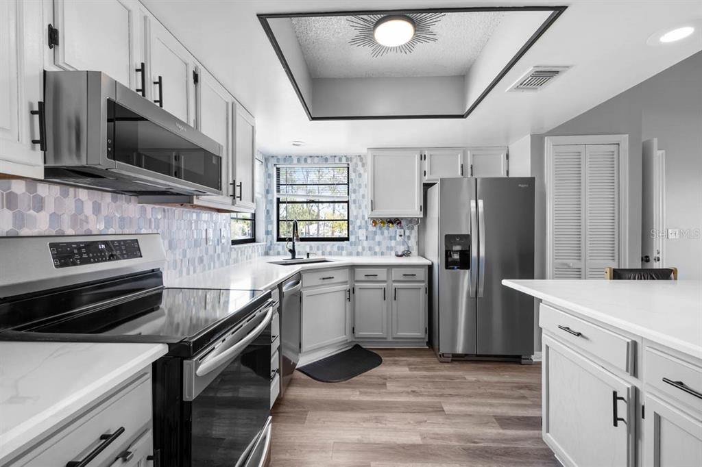 A modern kitchen features white cabinets, stainless steel appliances, a tile backsplash, and wood flooring — 609 LIVELY DRIVE UNIT B, SUN CITY CENTER, FL
