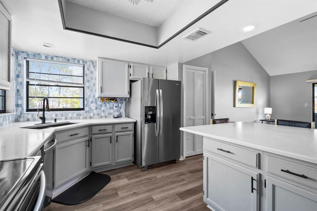 A kitchen features gray cabinets, white countertops, stainless steel appliances, and a blue tiled backsplash — 609 LIVELY DRIVE UNIT B, SUN CITY CENTER, FL