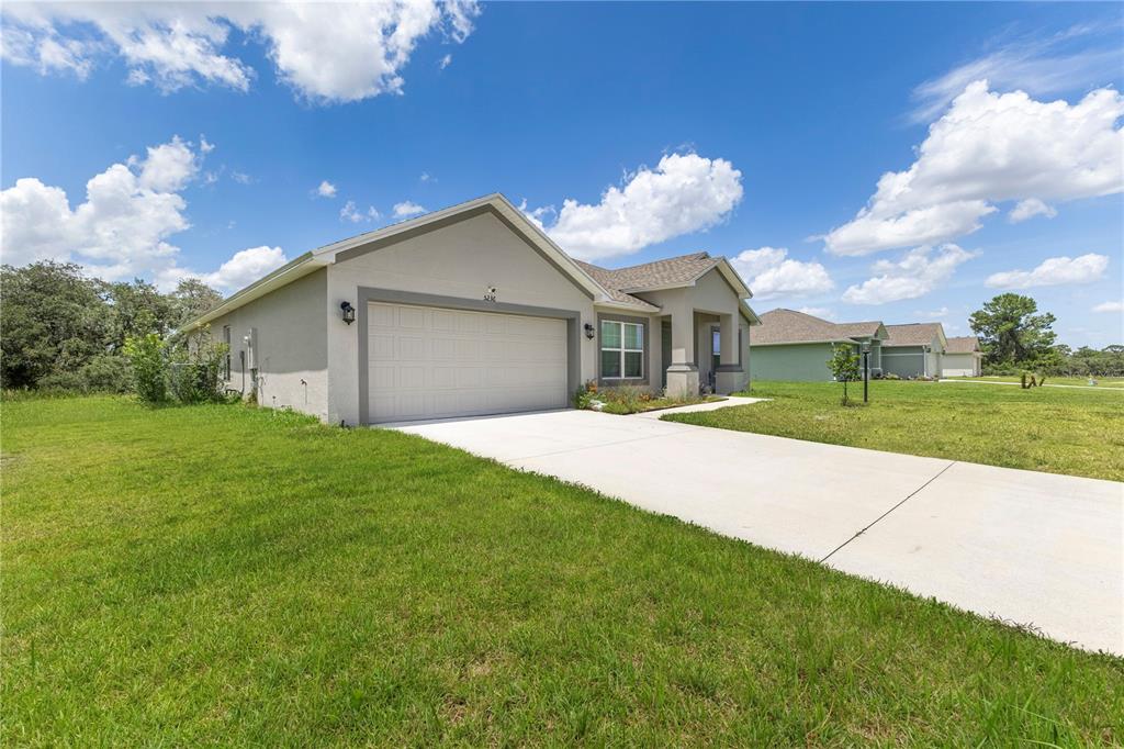 A single-story house with a two-car garage and a concrete driveway under a blue sky — 5236 SUE DRIVE, SEBRING, FL