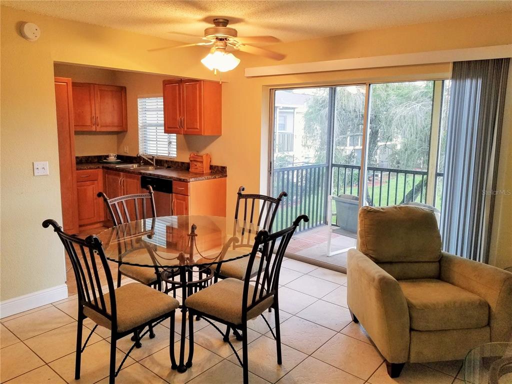 A dining area with a glass table and chairs sits adjacent to a kitchen and balcony — 13125 WILCOX ROAD UNIT 7203, LARGO, FL