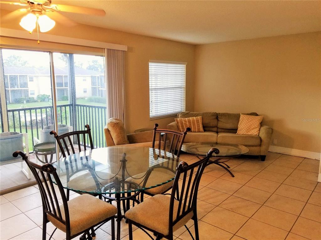 A dining area with a glass table and chairs sits before a living room sofa — 13125 WILCOX ROAD UNIT 7203, LARGO, FL