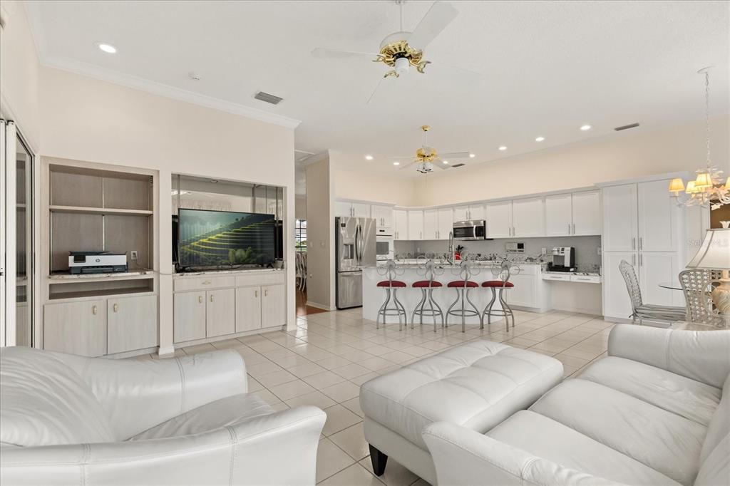 A bright open-concept living room and kitchen featuring white cabinetry, tiled floors, and leather furniture — 7103 MONTREAL DRIVE, LAKELAND, FL