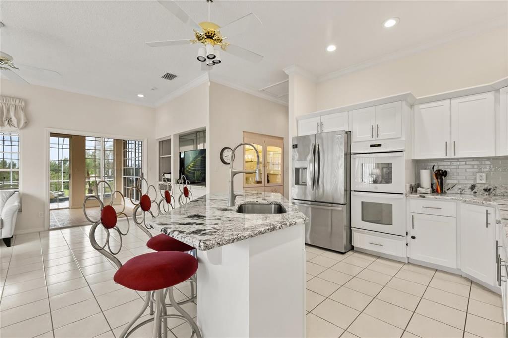 A kitchen features white cabinets, granite countertops, a center island with bar stools, and tile flooring — 7103 MONTREAL DRIVE, LAKELAND, FL