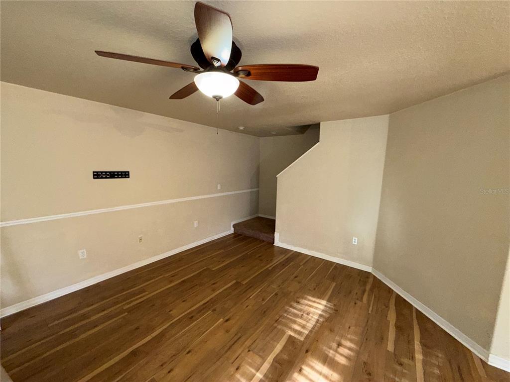An empty room features wood-look flooring, a ceiling fan, and a staircase leading upward — 37603 DALIHA TERRACE, ZEPHYRHILLS, FL