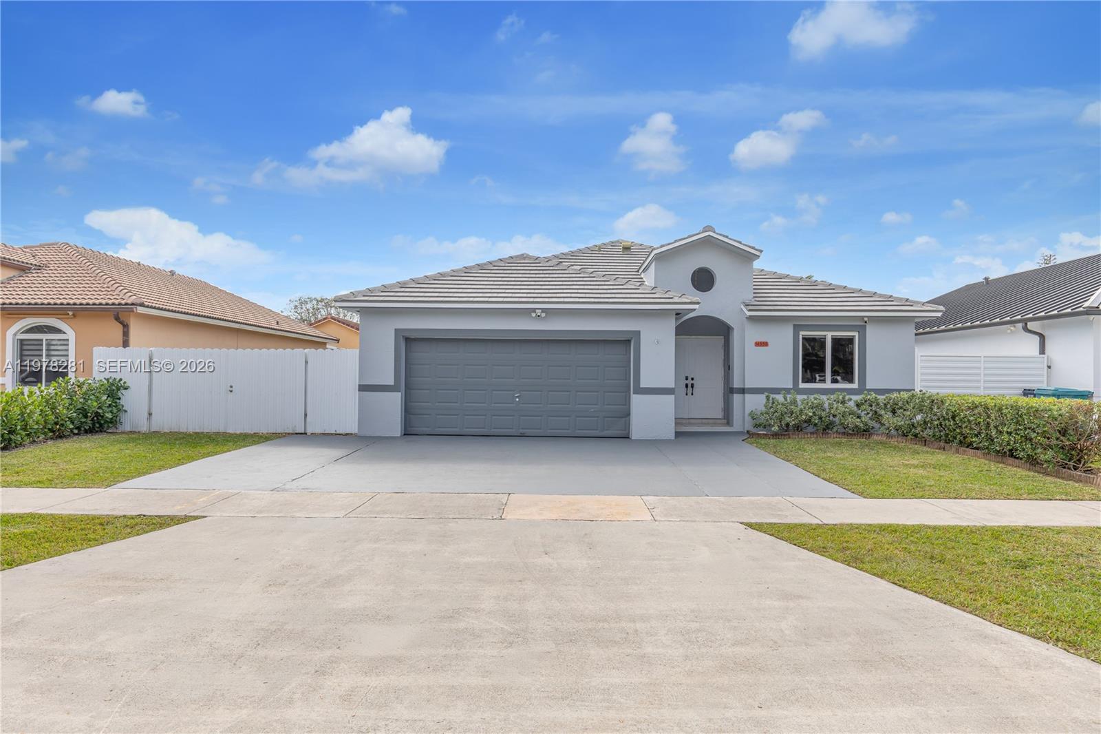 A single-story gray house features a two-car garage, a tiled roof, and a front lawn — 14358 SW 168th St, Miami FL 33177, MIAMI, FL