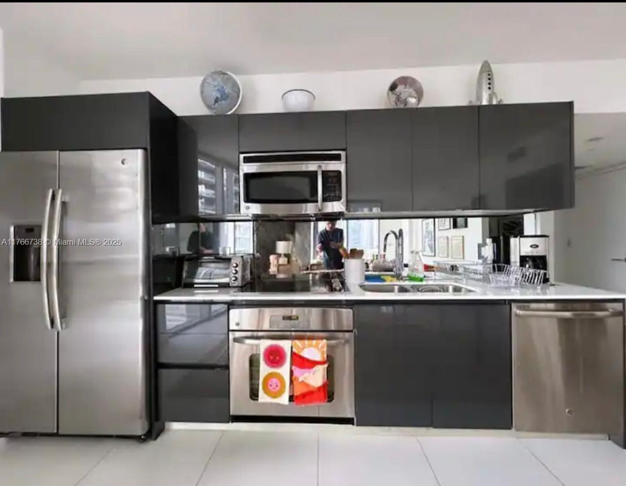 A modern kitchen features dark gray cabinetry, stainless steel appliances, and a mirrored backsplash — 31 SE 6th St # 1601, Miami FL 33131, MIAMI, FL
