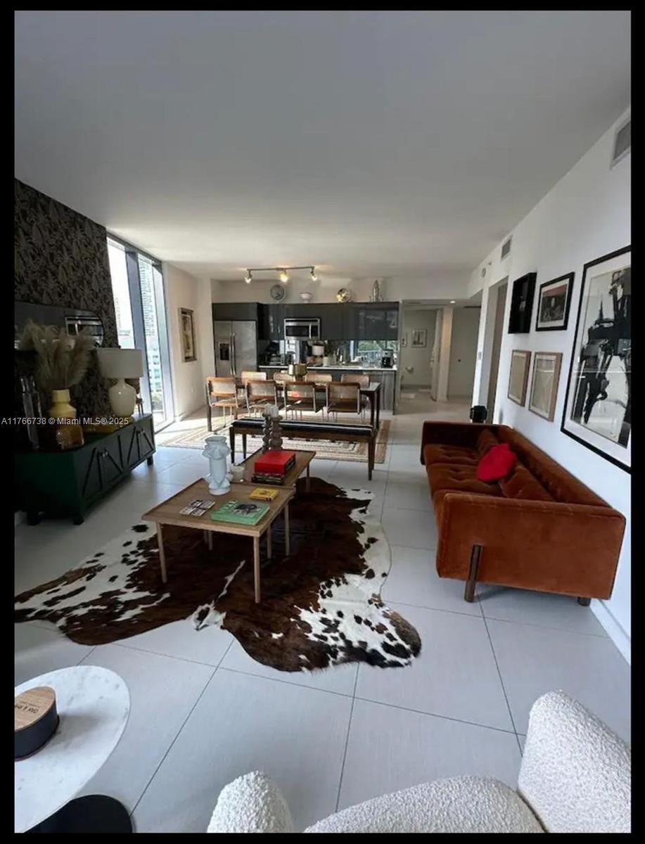 An open-concept living and dining area features a velvet sofa, cowhide rug, and modern kitchen — 31 SE 6th St # 1601, Miami FL 33131, MIAMI, FL