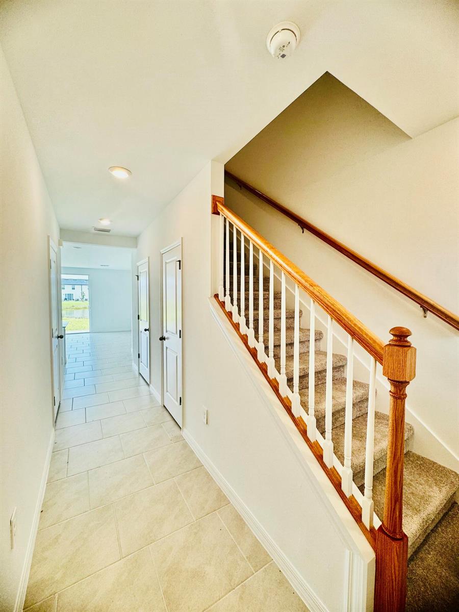 A hallway with tile flooring leads to a doorway, alongside a carpeted staircase with railings — 4264 Cirella Court, FL 33917, FL