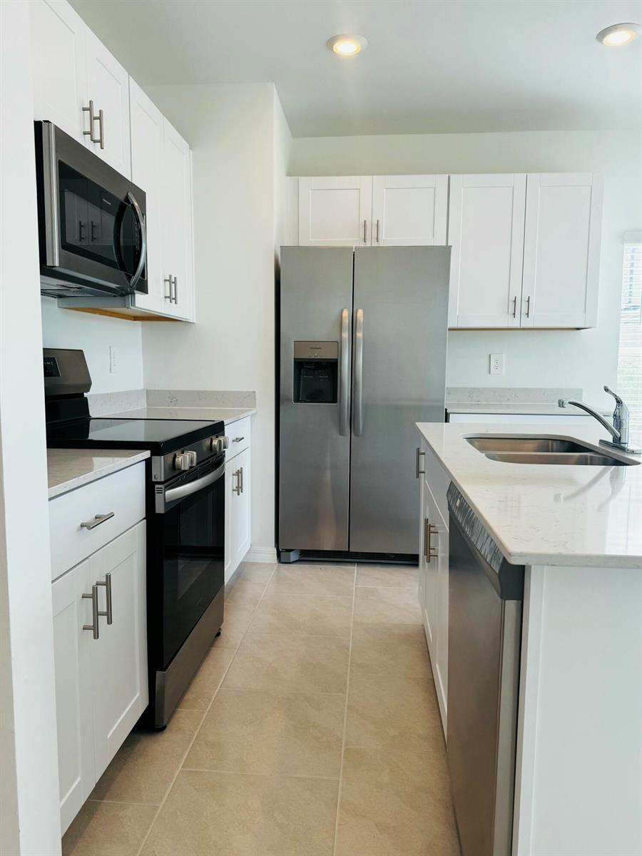 A kitchen features white cabinets, stainless steel appliances, a kitchen island, and light-colored tile flooring — 4264 Cirella Court, FL 33917, FL