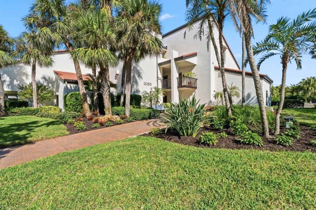 A two-story stucco building with a tiled roof, palm trees, and a paved walkway — 2055 GULF OF MEXICO DRIVE UNIT G2-213, LONGBOAT KEY, FL
