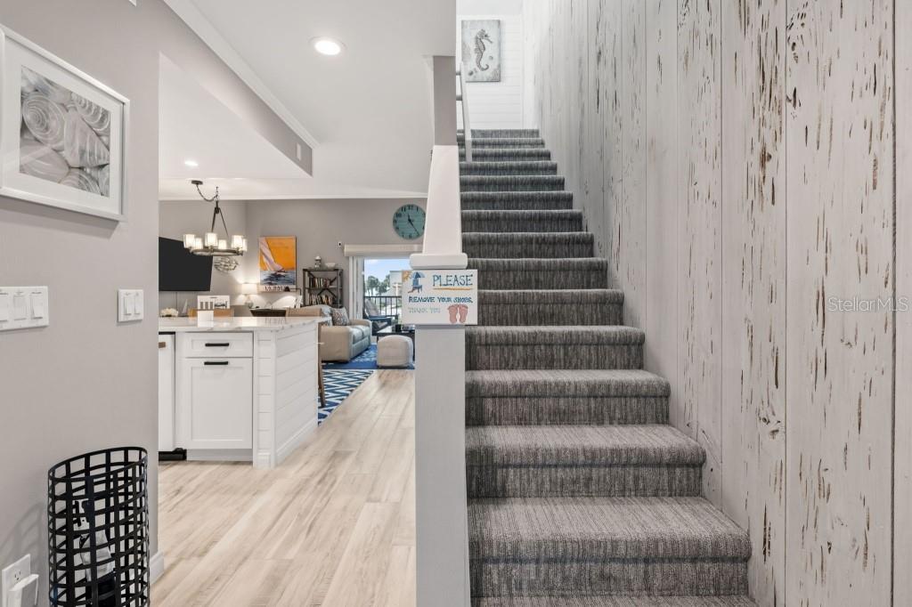 A staircase with gray carpet leads upward next to a kitchen and living area — 2055 GULF OF MEXICO DRIVE UNIT G2-213, LONGBOAT KEY, FL