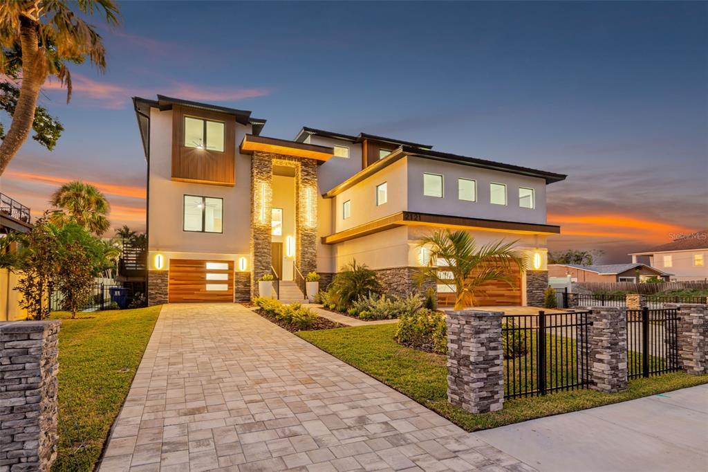A modern three-story house with a stone facade, wood accents, and a paved driveway at dusk — 2121 BAYOU GRANDE BOULEVARD NE, ST PETERSBURG, FL