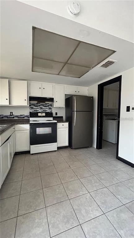 A kitchen features white cabinetry, a black stove, a stainless steel refrigerator, and tiled floors — 2235 SILVER PINES PLACE UNIT 401, ORLANDO, FL