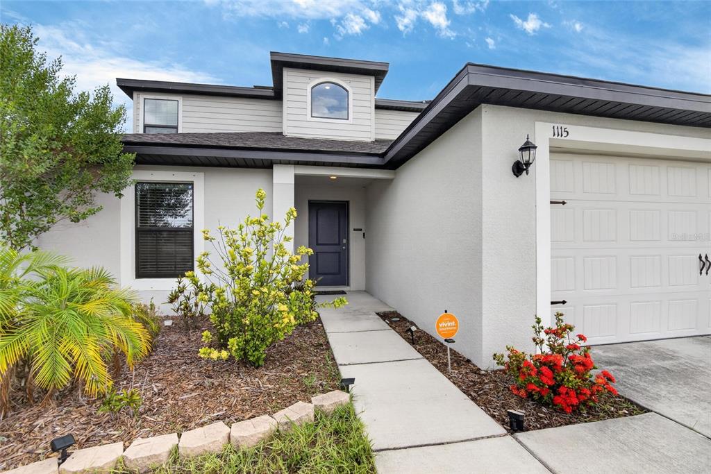 A two-story house exterior with a gray front door, a garage, and a concrete walkway — 1115 WYNNMERE WALK AVENUE, RUSKIN, FL