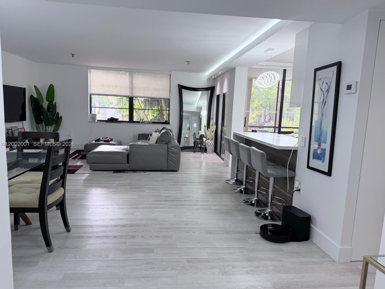 An open-concept living and dining area features light wood flooring, a breakfast bar, and furniture — 671 NE 195th St # 208E, Miami FL 33179, MIAMI, FL
