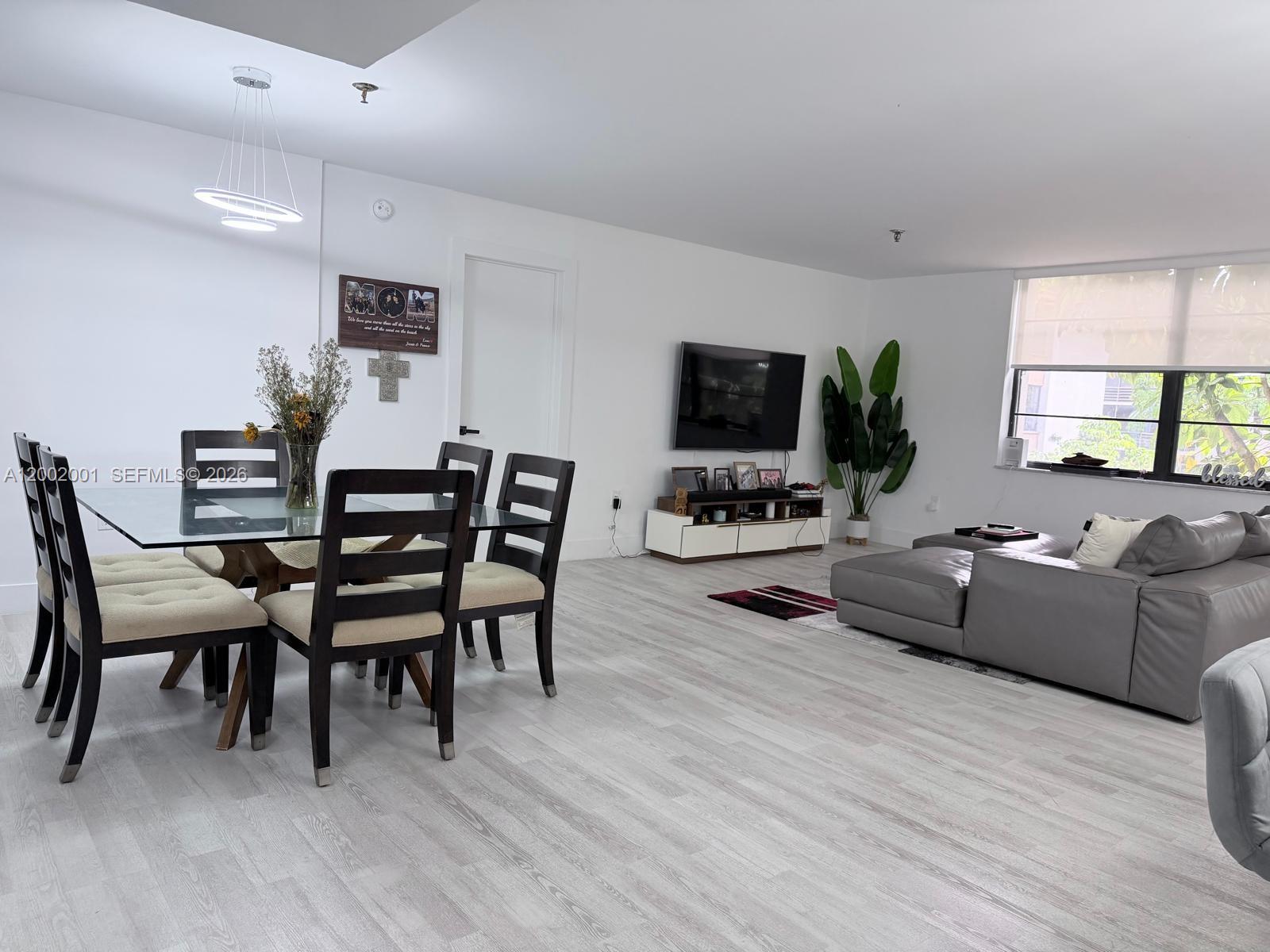 An open-concept living and dining area features light wood-look flooring, a glass dining table, and a sectional sofa — 671 NE 195th St # 208E, Miami FL 33179, MIAMI, FL