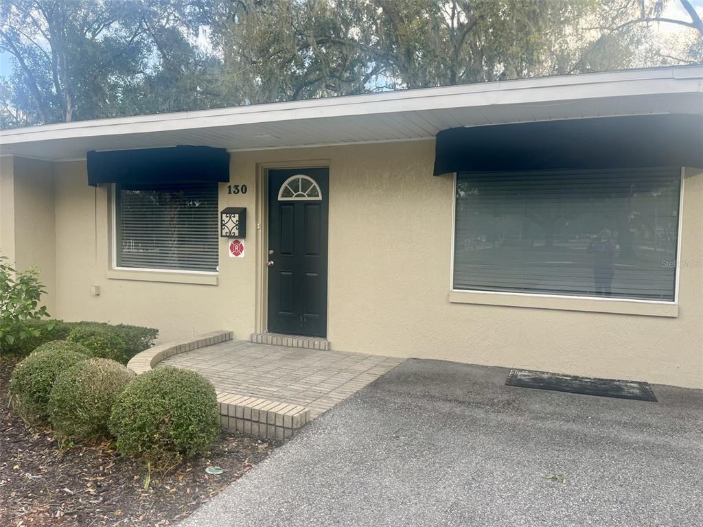 The exterior of a single-story building features a black front door, two windows, and landscaping — 130 E 1ST STREET, APOPKA, FL