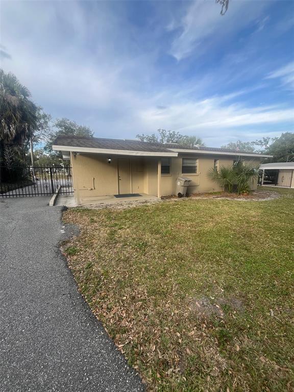 A tan, single-story house exterior features a covered entryway, a driveway, and a metal gate — 130 E 1ST STREET, APOPKA, FL