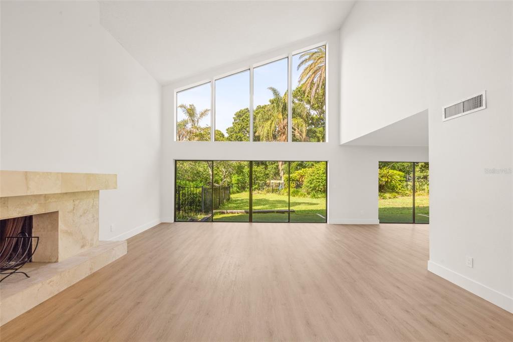 A living room with light wood floors, a stone fireplace, and large floor-to-ceiling windows — 2668 CONCORDE COURT, CLEARWATER, FL