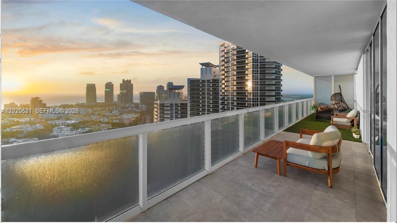 A high-rise balcony features a glass railing, tiled flooring, and outdoor seating overlooking a city — 450 Alton Rd # 2810, Miami Beach FL 33139, MIAMI BEACH, FL