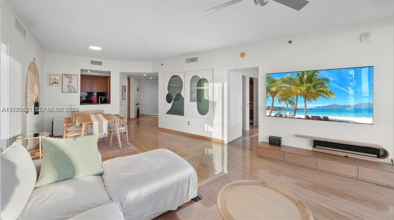 A living room features light wood flooring, a large wall-mounted television, and an adjacent dining area — 450 Alton Rd # 2810, Miami Beach FL 33139, MIAMI BEACH, FL