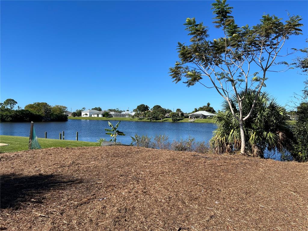 A view of a lake from a mulched yard with a tree and distant houses — 145 ROBINA STREET, PORT CHARLOTTE, FL