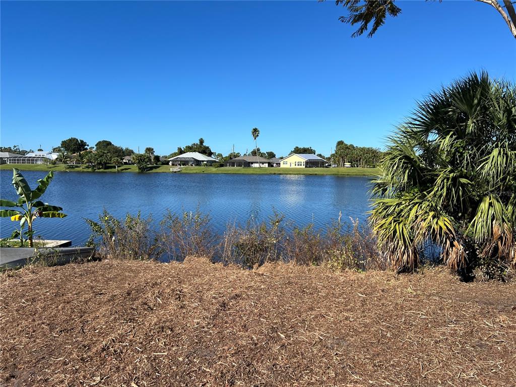 A view of a lake from a dirt lot with palm trees and houses beyond — 145 ROBINA STREET, PORT CHARLOTTE, FL