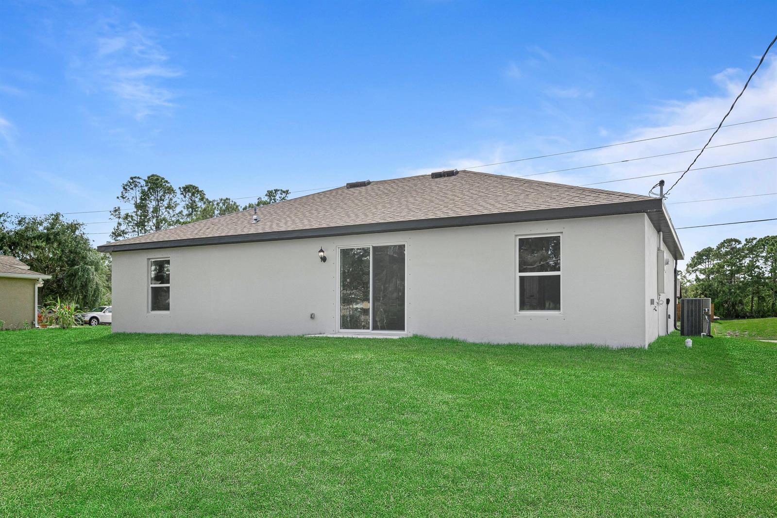 The rear exterior of a single-story house features a sliding glass door and two windows — 9350 104th Court, Vero Beach FL 32967, VERO BEACH, FL
