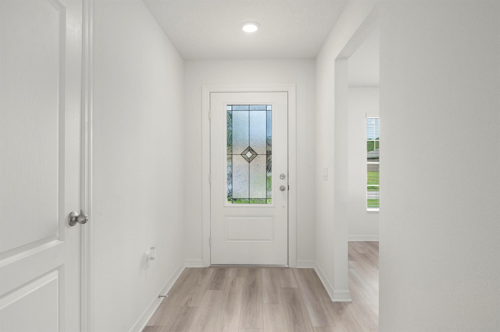 A bright entryway features light wood-look flooring, white walls, and a front door with glass — 9350 104th Court, Vero Beach FL 32967, VERO BEACH, FL
