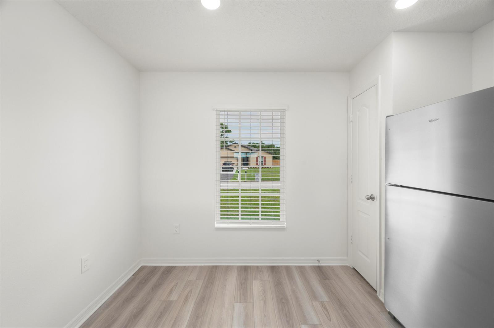A bright, empty room with white walls, light wood-look flooring, a window, and a refrigerator — 9350 104th Court, Vero Beach FL 32967, VERO BEACH, FL