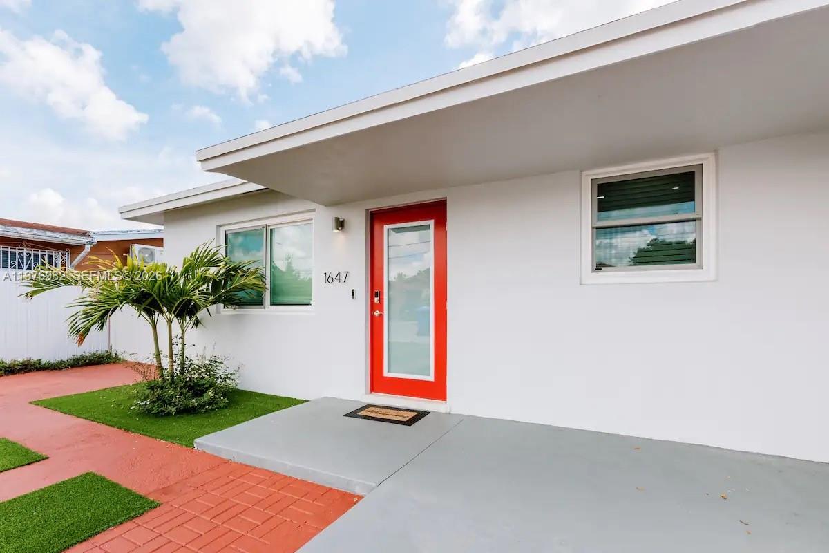 The exterior of a white house features a bright red front door and a palm tree — 1647 NW 29th Ave, Miami FL 33125, MIAMI, FL