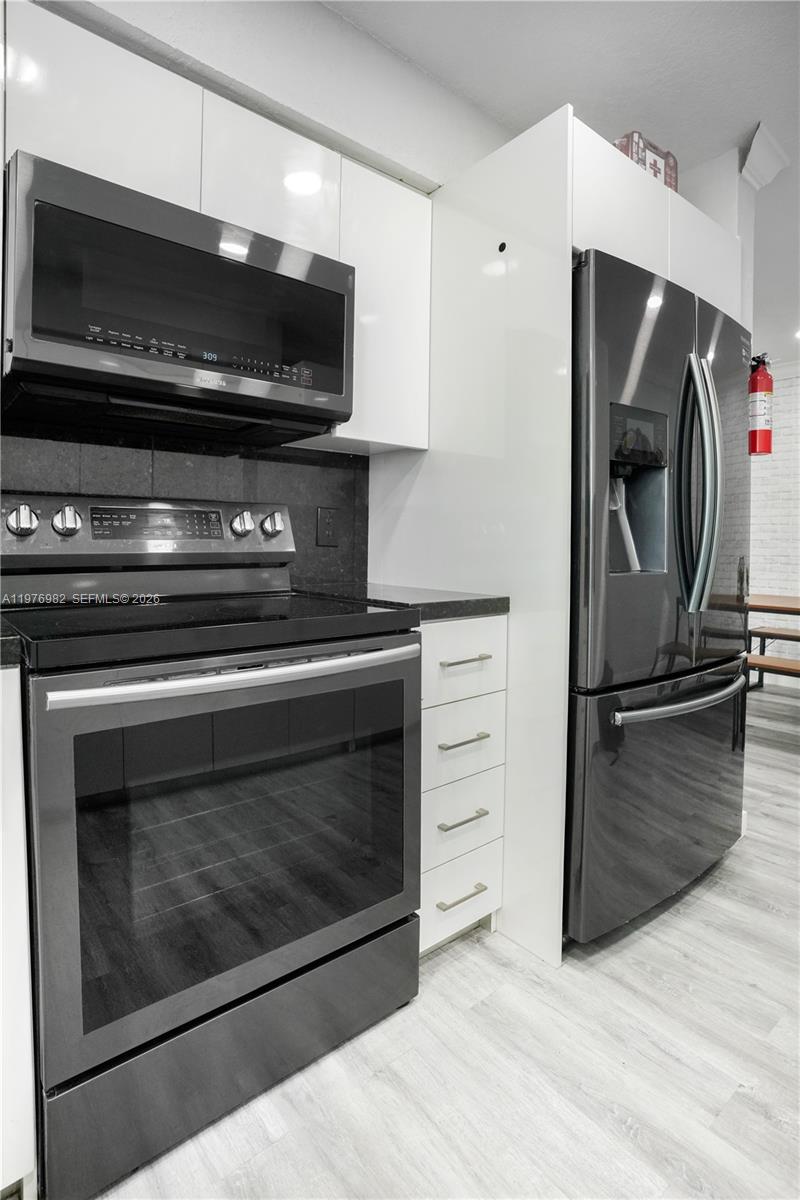 A kitchen features dark stainless steel appliances, white cabinets, and light wood-look flooring — 1647 NW 29th Ave, Miami FL 33125, MIAMI, FL