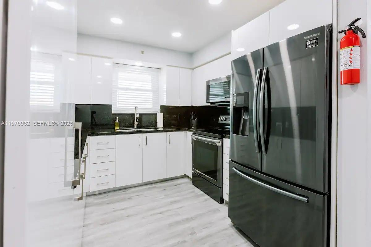 A modern kitchen features white cabinets, black countertops, stainless steel appliances, and light wood flooring — 1647 NW 29th Ave, Miami FL 33125, MIAMI, FL