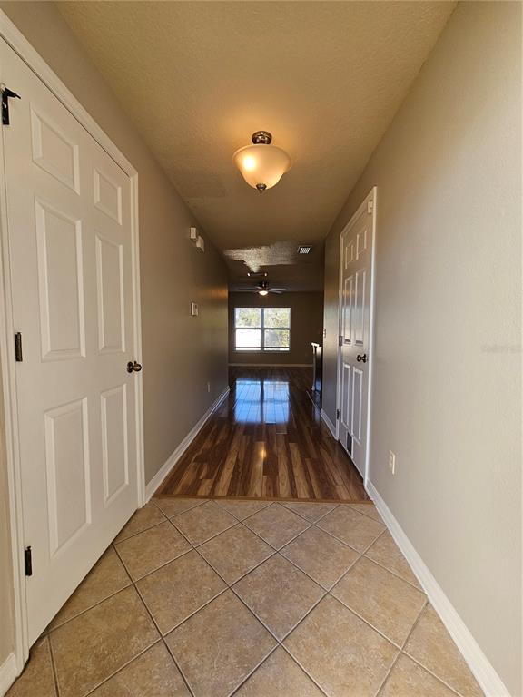 A hallway with tiled flooring transitions to wood flooring, leading toward a windowed living area — 2954 WILLOWLEAF LANE, WESLEY CHAPEL, FL