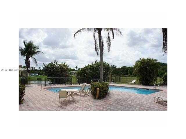 A swimming pool with a patio, lounge chairs, and palm trees in a fenced area — DAVIE, FL