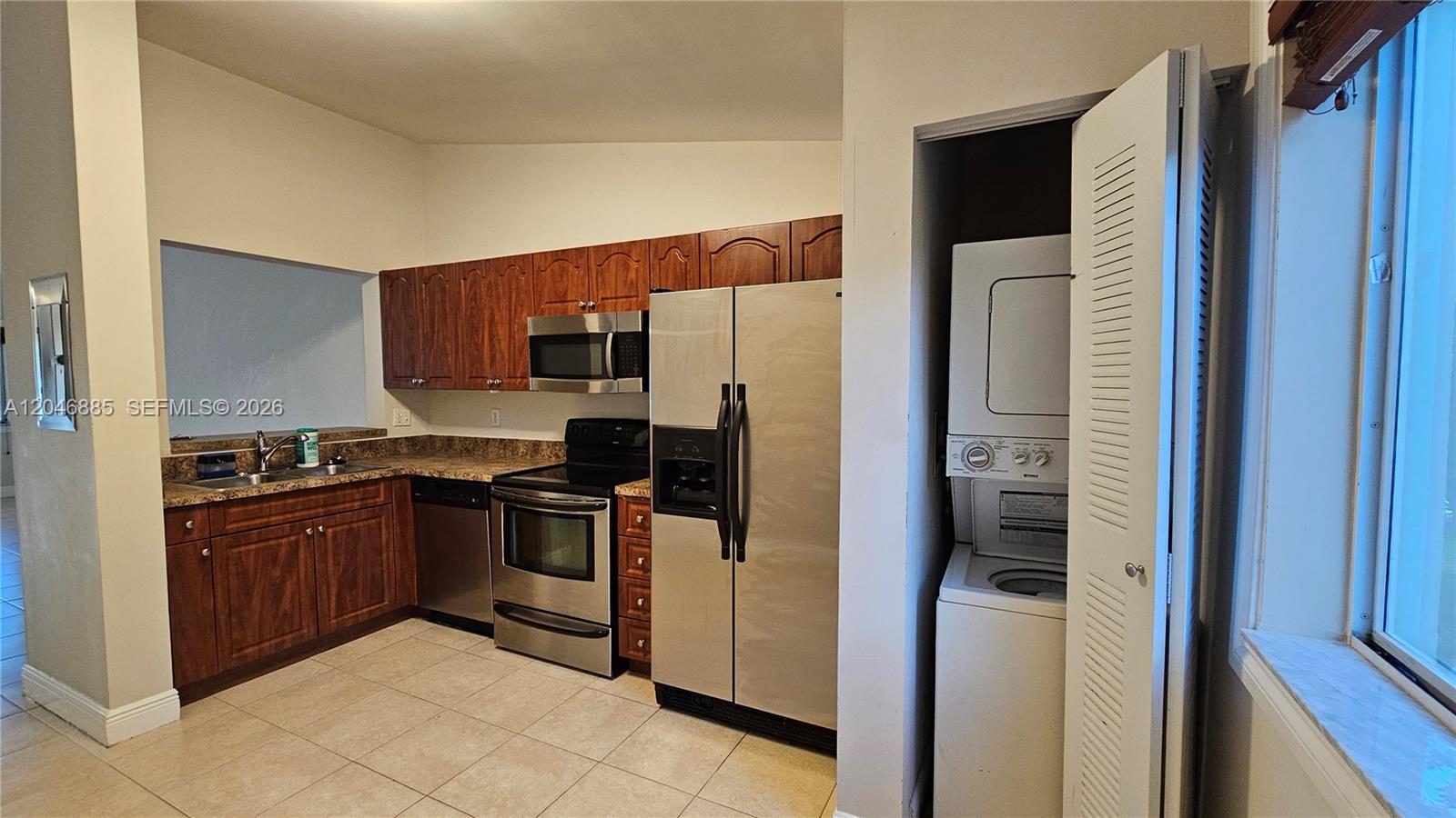 A kitchen features wood cabinets, stainless steel appliances, tile flooring, and an adjacent laundry closet — DAVIE, FL