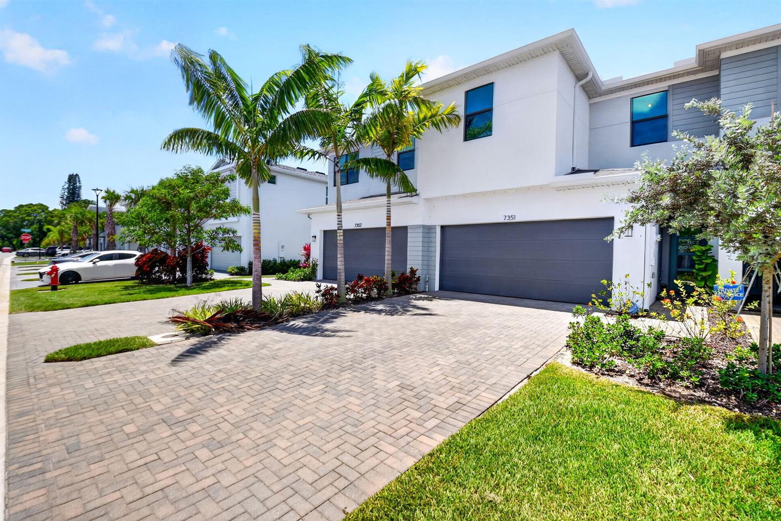 A modern two-story townhouse features a paved driveway, two garage doors, and palm trees — 7351 Lenora Lane, Lake Worth FL 33467, LAKE WORTH, FL