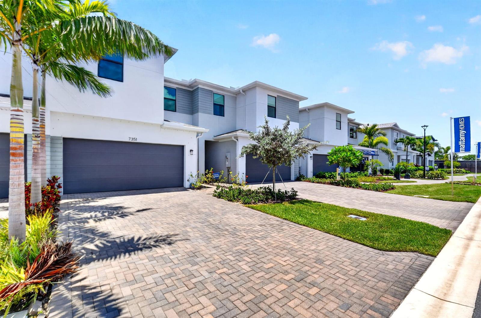 A row of modern townhomes features gray garage doors, paved driveways, and landscaped front yards — 7351 Lenora Lane, Lake Worth FL 33467, LAKE WORTH, FL
