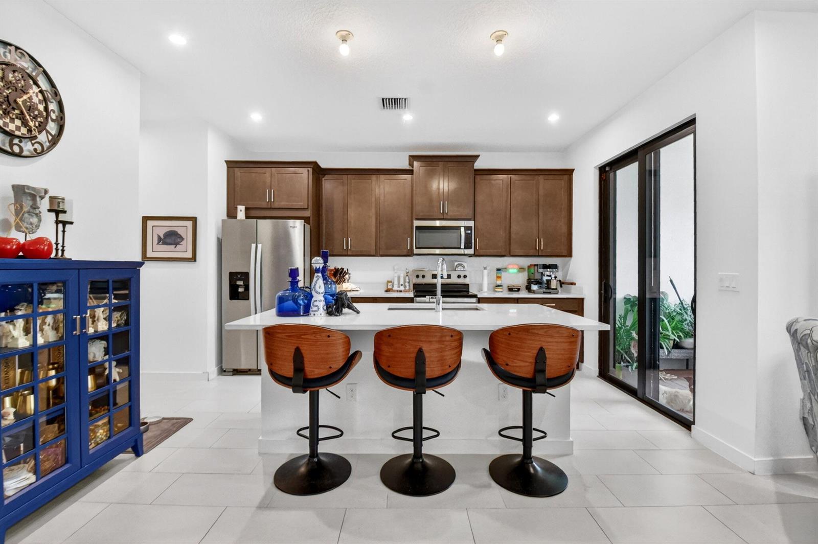 A kitchen features a white island with three wooden bar stools and dark wood cabinetry — 7351 Lenora Lane, Lake Worth FL 33467, LAKE WORTH, FL