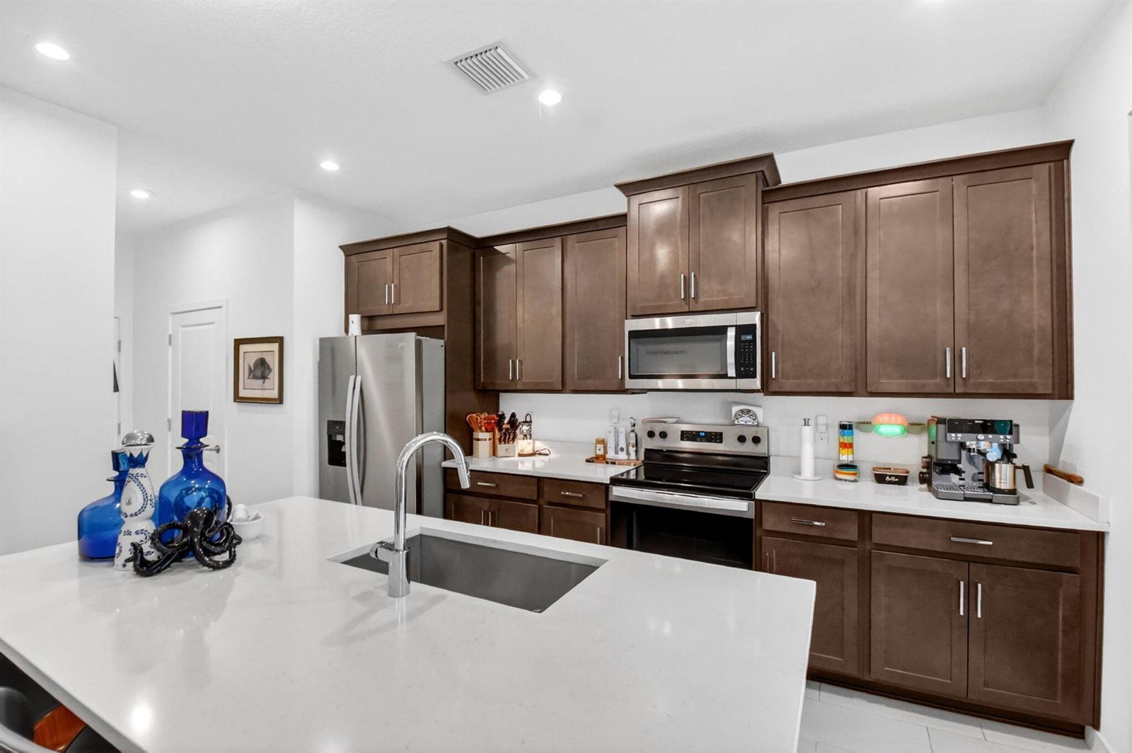 A kitchen features dark wood cabinets, white countertops, a central island with a sink, and stainless appliances — 7351 Lenora Lane, Lake Worth FL 33467, LAKE WORTH, FL