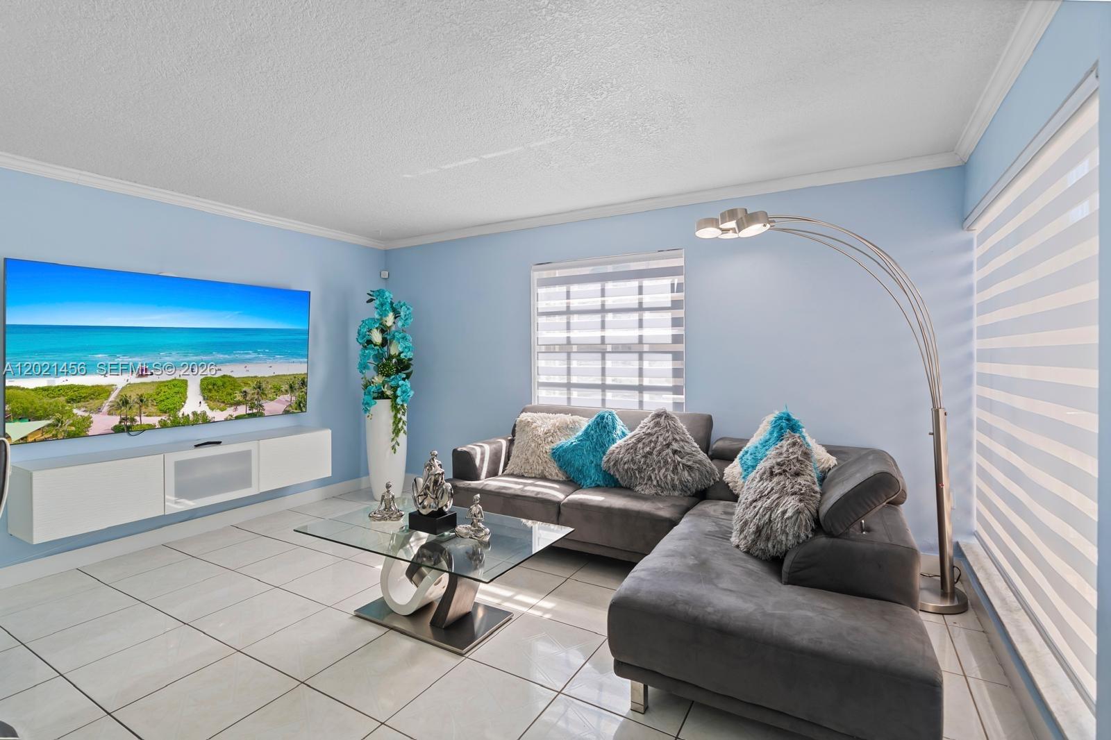 A living room features a grey sectional sofa, a glass coffee table, and a wall-mounted television — 11860 SW 18th Terr # 103, Miami FL 33175, MIAMI, FL