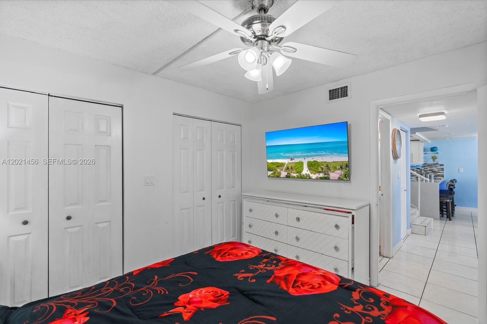A bedroom features a white dresser, a wall-mounted television, and a floral-patterned bedspread — 11860 SW 18th Terr # 103, Miami FL 33175, MIAMI, FL