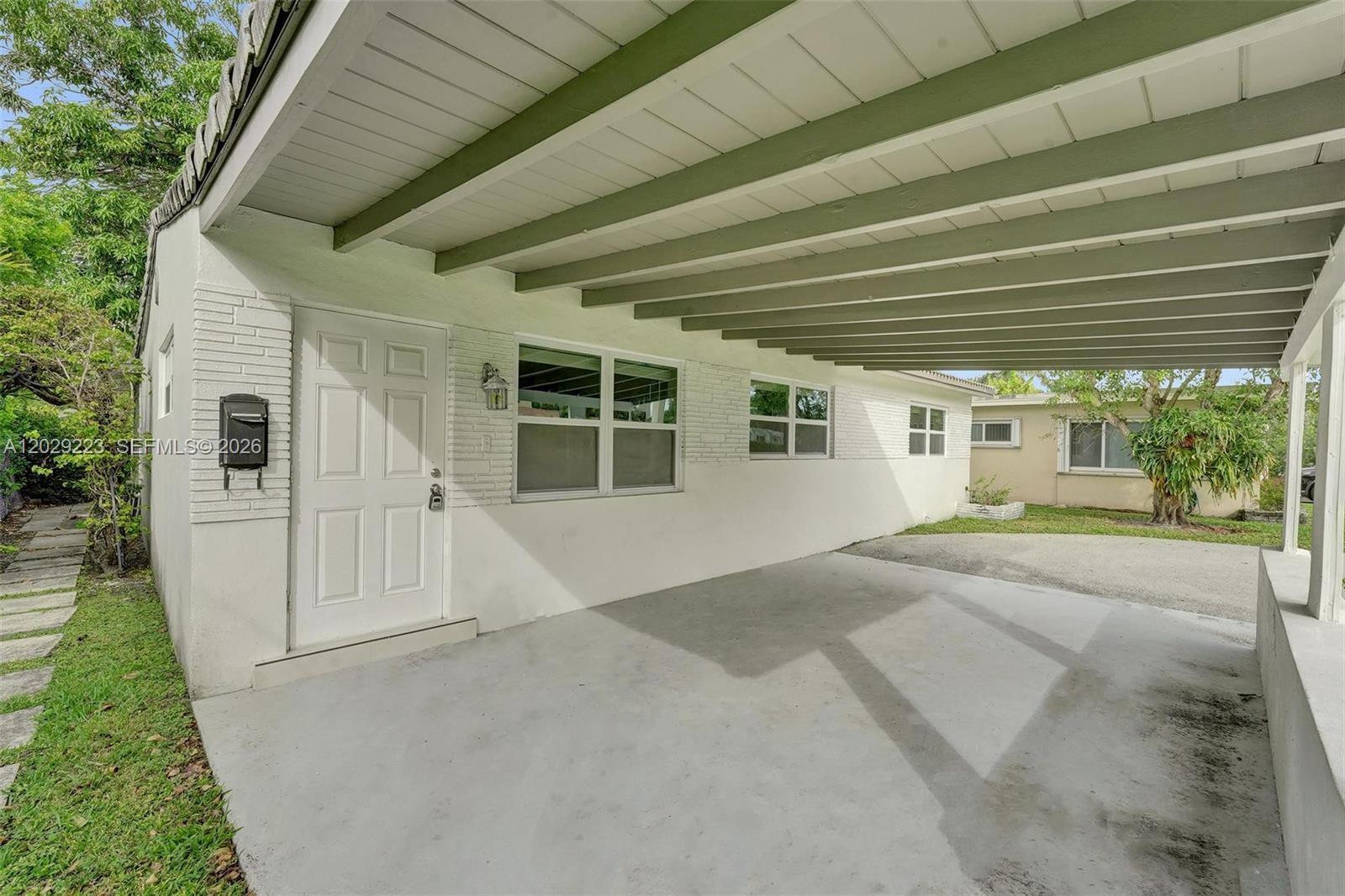 A white house exterior features a covered carport with exposed beams and a front door — 1423 Garfield St, Hollywood FL 33020, HOLLYWOOD, FL