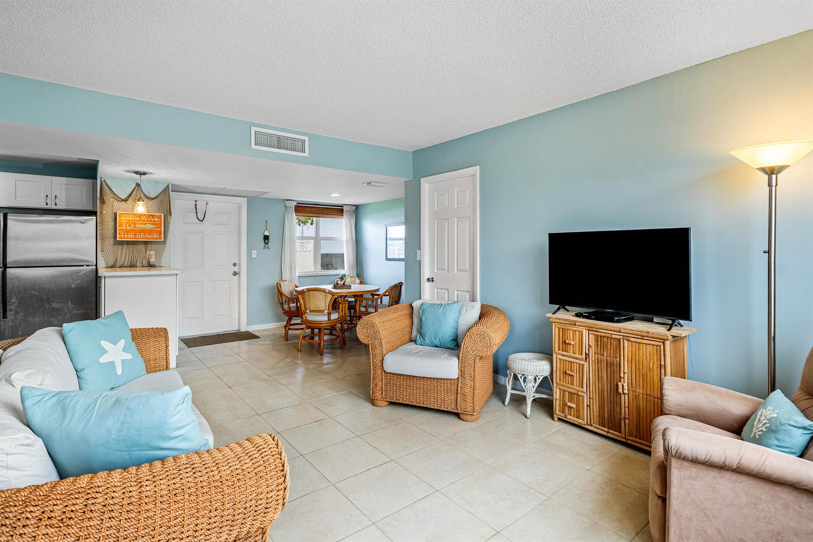 A living room with light blue walls, tile flooring, wicker furniture, and a television console — 1820 New Palm Way # 103, Boynton Beach FL 33435, BOYNTON BEACH, FL