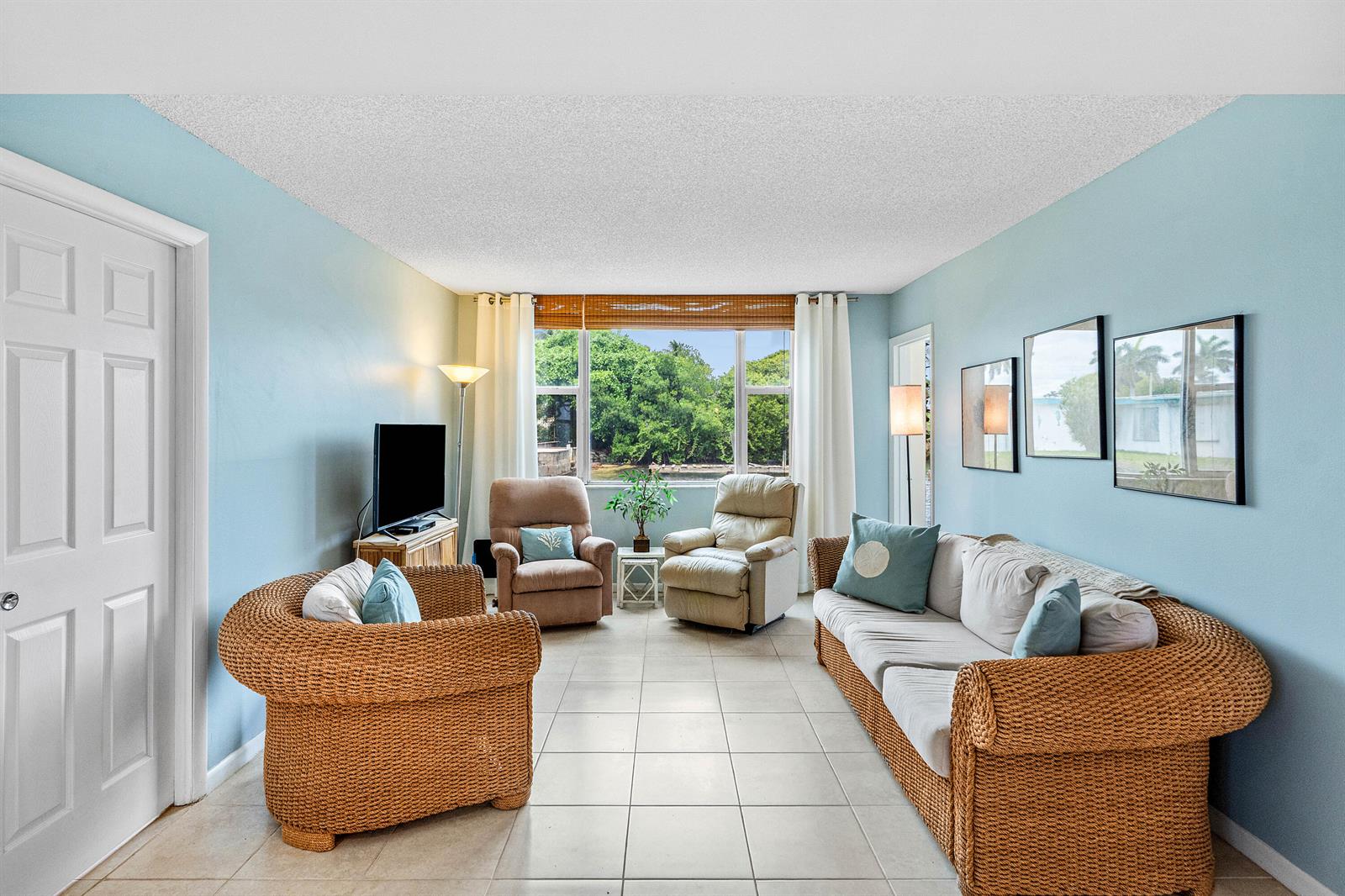A living room with light blue walls, tile flooring, wicker furniture, and a large window — 1820 New Palm Way # 103, Boynton Beach FL 33435, BOYNTON BEACH, FL